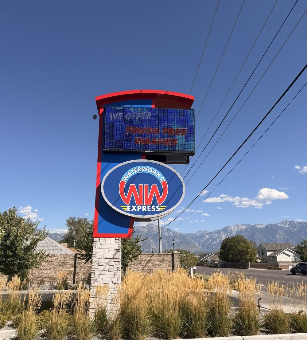 The WaterWorks Express road sign on 7800 South, with the logo below an LED board reading We offer touch free washes, and the Wasatch mountains behind.