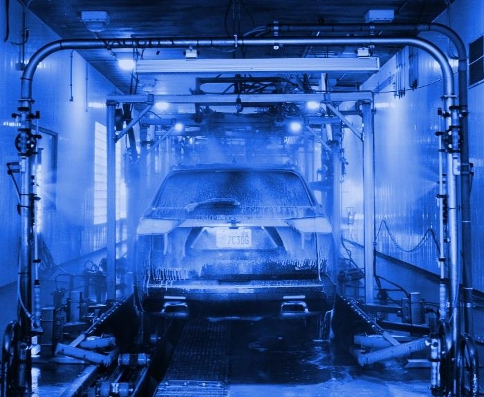 A car being washed inside the 180-foot tunnel at WaterWorks Express on 9000 South, lit blue, with foam and high-pressure rinse arches on both sides.
